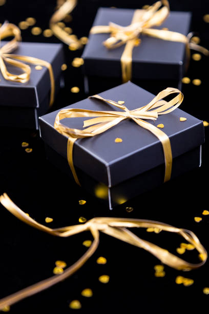 istock Black gift boxes with gold ribbon on shine background. Close up. 890931942
