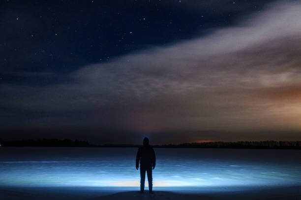 istock A man with a flashlight on his head is standing and looking at the beautiful starry sky with clouds. In a snowy field. Winter, a frosty night. 890935472