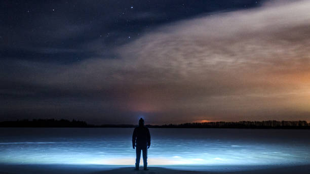 istock A man with a flashlight on his head is standing and looking at the beautiful starry sky with clouds. In a snowy field. Winter, a frosty night. 890935480