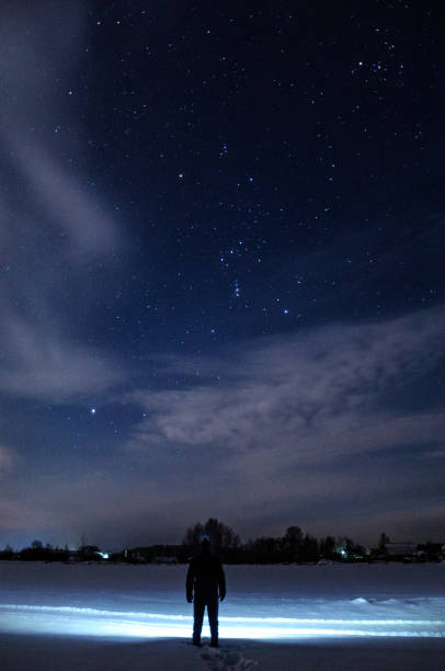 istock A man with a flashlight on his head is standing and looking at the beautiful starry sky with clouds. In a snowy field. Winter, a frosty night. 890935522
