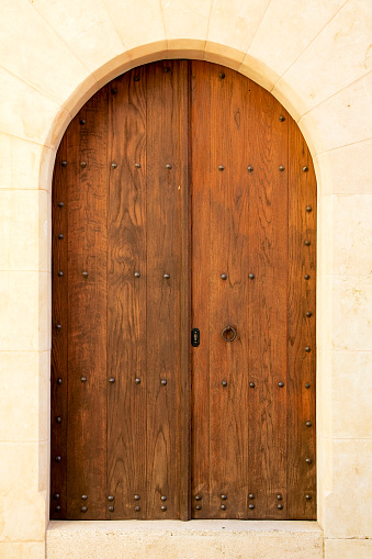 Antique, dark brown external double door in stone, arched portal.