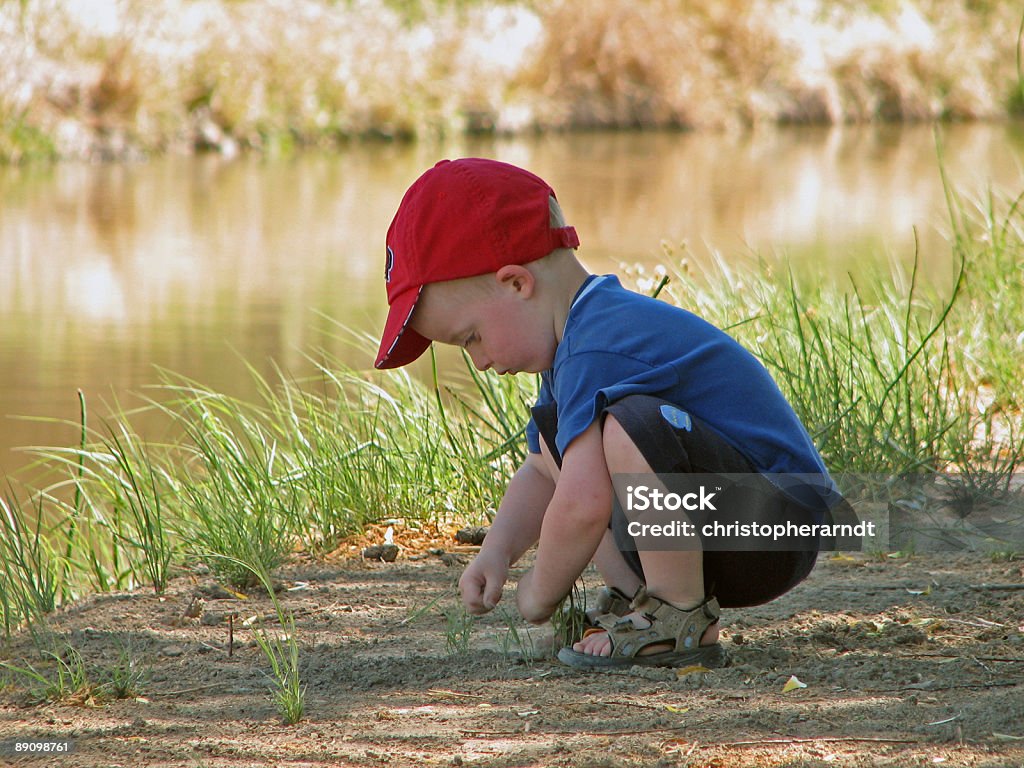 Jeune garçon soulever rochers près de l'eau - Photo de Casquette de baseball libre de droits