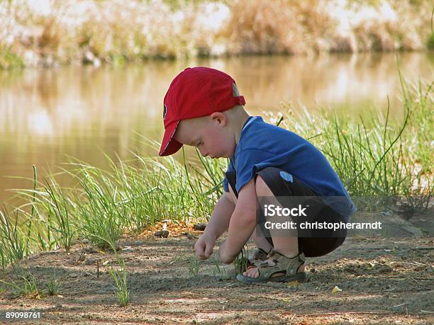 Photo libre de droit de Jeune Garçon Soulever Rochers Près De Leau banque d'images et plus d'images libres de droit de Casquette de baseball - Casquette de baseball, Petits garçons, Vue latérale