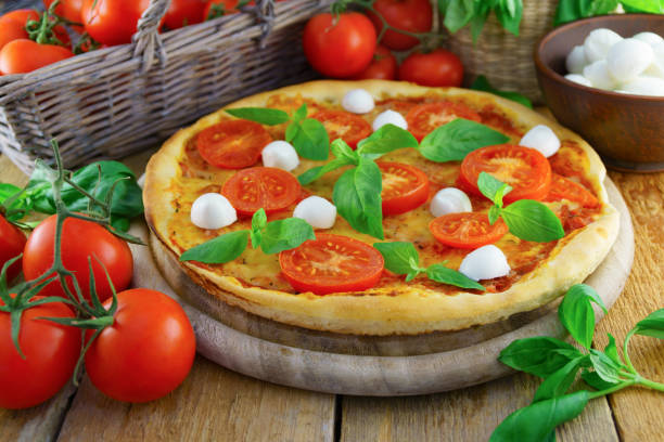 istock Italian pizza with mozzarella, cheese, and basil leaves on rough rustic rural planks table. Wicker wooden basket with fresh raw organic tomatoes. Horizontal, selective focus. 890994466