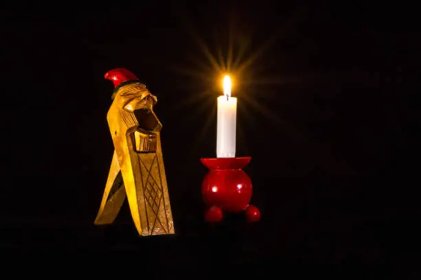 A Norwegian Gnome Handcarved Wooden Nut Cracker together with a candlelight on a typical red wooden candlestick  a still life.