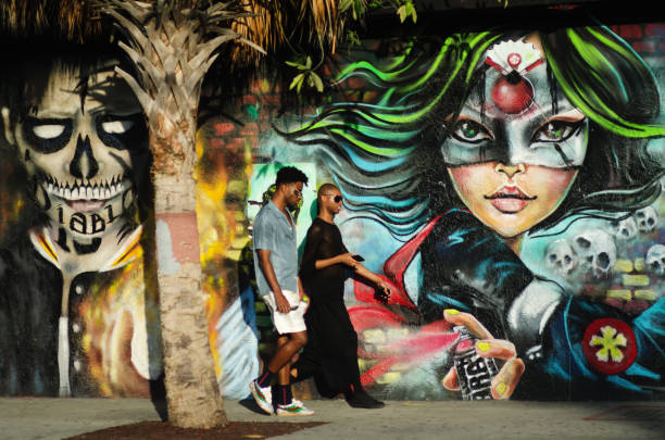 A pair of fashionistas walk past a wall of colorful graffiti on a visit to the Wynwood Arts District during Art Basel Miami Beach 2017