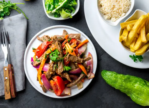 Peruvian dish Lomo saltado - beef tenderloin with purple onion, yellow chili, tomatoes served on white plate with french fries and rice. Top view