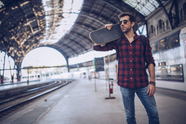 istock Hipster man with skateboard waiting a train 891144760