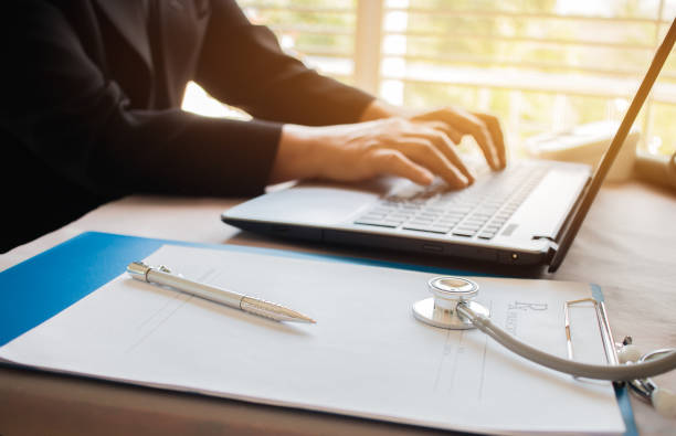 istock Doctor's working on laptop computer, writing prescription clipboard with record information paper folders on desk in hospital or clinic, Healthcare and medical concept. Focus on stethoscope 891153186