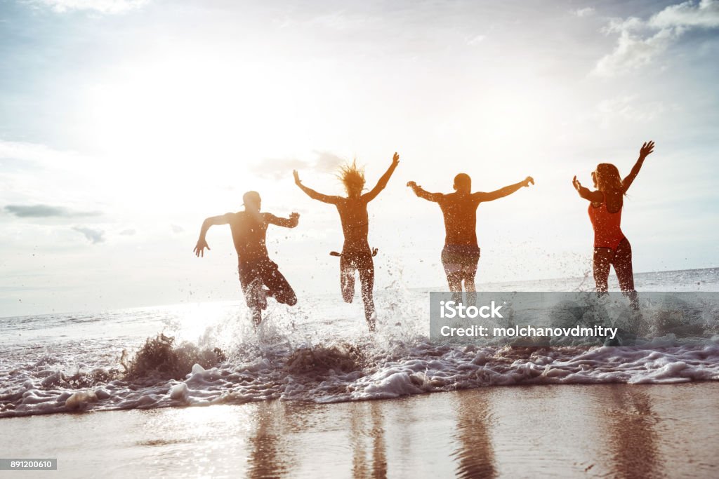 Four happy friends runs to sunset beach Four happy friends having fun and runs to sunset sea beach. Space for text Beach Stock Photo