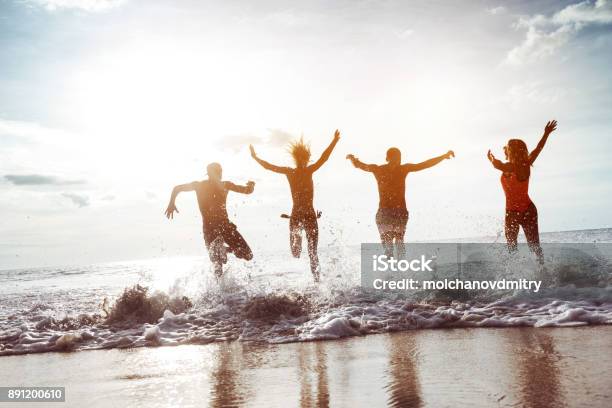 Four Happy Friends Runs To Sunset Beach Stock Photo - Download Image Now - Beach, Friendship, Running