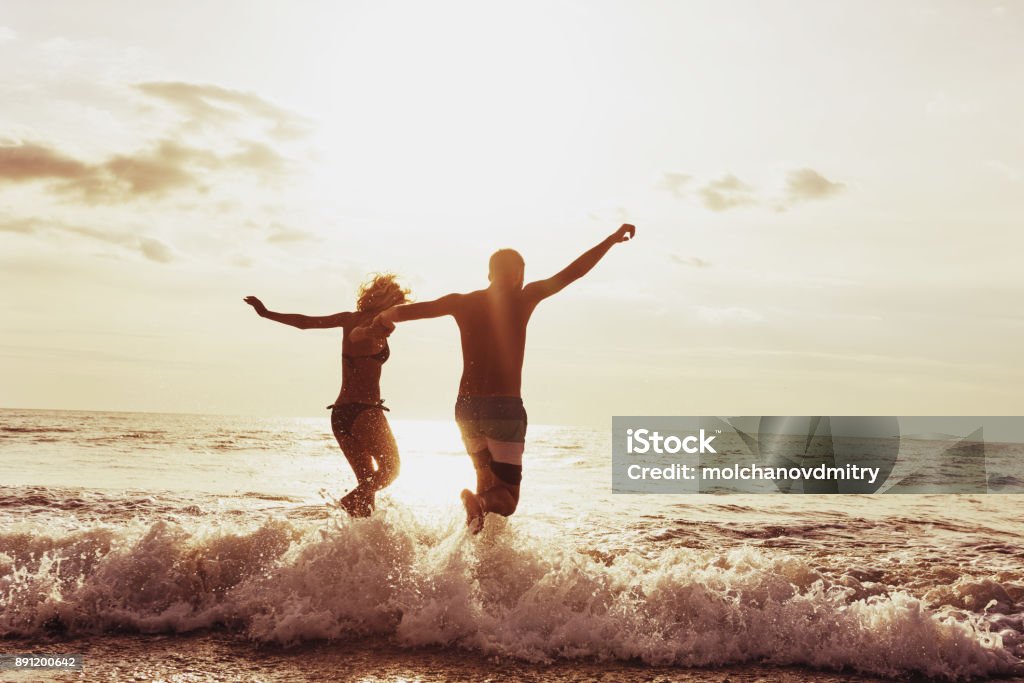 Happy couple sunset beach run Happy couple having fun and jumps to sunset sea. Beach travel concept Couple - Relationship Stock Photo