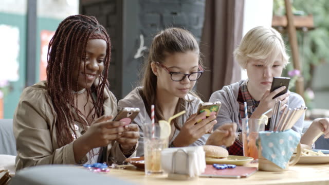 Teenage Girls Texting on Smartphones in Outdoor Cafe