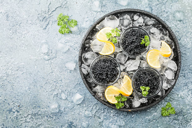 Black caviar on ice Black caviar in a glass bowl on ice with lemon close up over gray background, top view caviar stock pictures, royalty-free photos & images