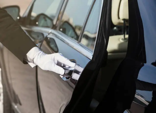 The white gloved hand of a uniformed chauffeur / doorman opening / closing a car door.