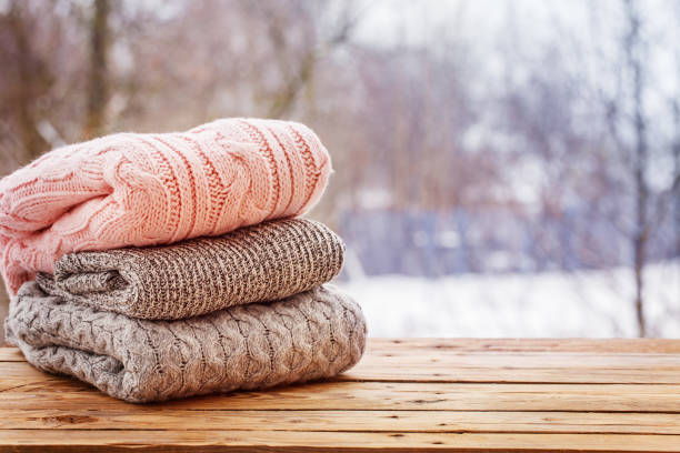 Stos złożonych, teksturowanych swetrów na drewnianej powierzchni na śnieżnym tle na świeżym powietrzu, idealny do stylu marynistycznego.
