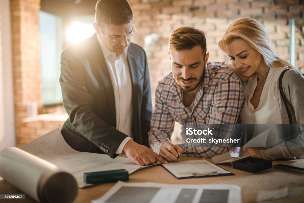 Sign here and the apartment is yours! Mid adult investor showing young couple where to sign the contract for buying a house. Building Contractor Stock Photo