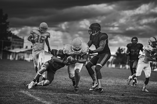 Determined American football player making a touchdown while passing through defensive players on playing field. Black and white photography.