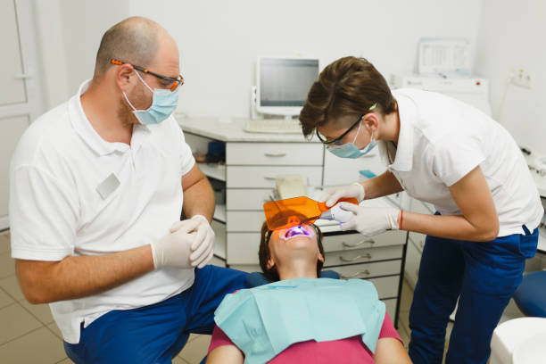 ホワイトニング uv 感光性樹脂組成物とのプロセス。プロの歯科医師と女性アシスタント クリニック最新のツール装備軽負荷のオフィスで女性患者の歯の治療に役立ちます。 - dental light dental equipment hospital professional occupation ストックフォトと画像
