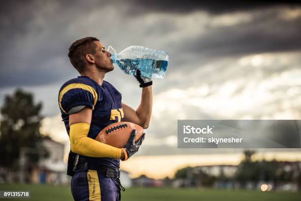 Thirsty American Football Player Drinking Fresh Water On Playing Field Stock Photo - Download Image Now