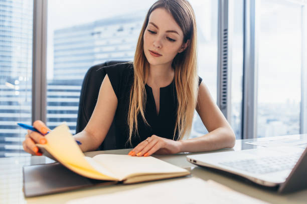 istock Confident female entrepreneur planning her workday sitting at her desk holding pen thinking looking at notebook in office 891318318