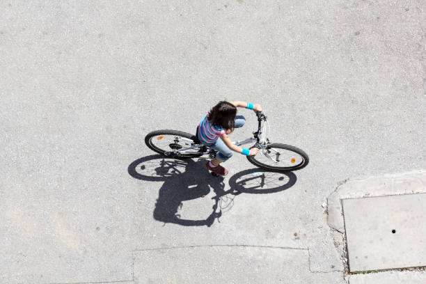 istock Little girl riding a bicycle on asphalt, long shadow, top view 891326676