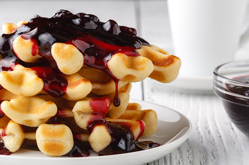Stock photo showing close-up, elevated view of blue rimmed plate containing breakfast of homemade Belgian waffle squares topped with natural yoghurt, cherries and blueberries, dusted with icing sugar.