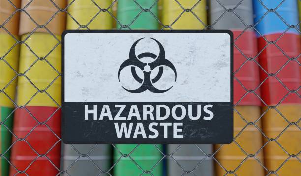 hazardous waste sign on chain link fence. oil barrels in background. 3d rendered illustration. - medical waste imagens e fotografias de stock