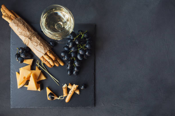 plato de quesos, servido con galletas, uvas y copa de vino blanco sobre fondo oscuro. - dessert buffet italian culture food fotografías e imágenes de stock