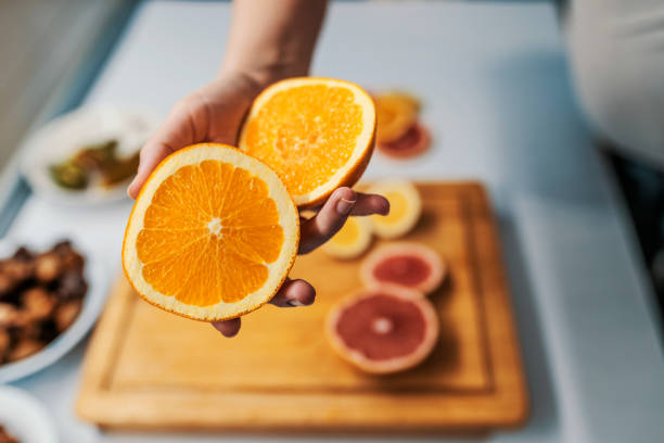 Offering you an orange Female hand  holding fresh Orange in her kitchen. Home grown ripe clementines, organic food that the girl holds in her hand. Woman holding two halves of Orange citrus fruit 2017 photos stock pictures, royalty-free photos & images