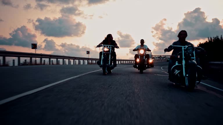 Young male bikers riding motorcycles on highway at sunset