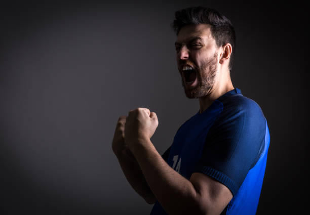 istock Male athlete / fan in blue uniform celebrating on white background 891394874