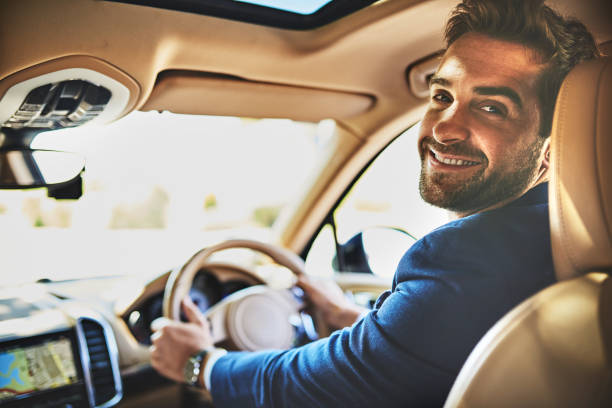 Portrait of a cheerful young businessman driving in his car to work while sitting in traffic and looking into the camera