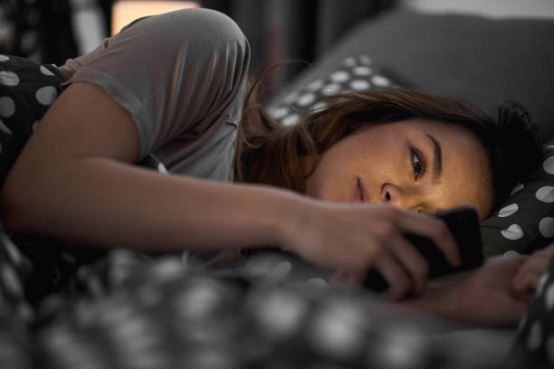 girl using smart phone and lying down in bed - internet dating imagens e fotografias de stock