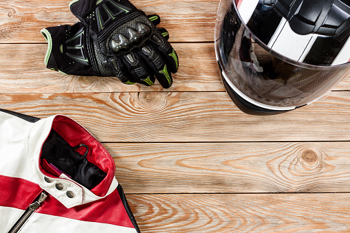 Overhead view of biker accessories placed on rustic wooden table. Items included motorcycle helmet, gloves and jacket. Motorcycle travel dream concept.