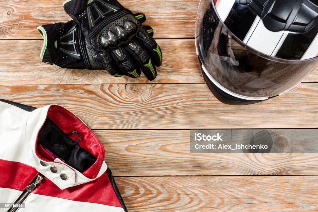 View of motorcycle rider accessories placed on rustic wooden table. Overhead view of biker accessories placed on rustic wooden table. Items included motorcycle helmet, gloves and jacket. Motorcycle travel dream concept. Motorcycle Stock Photo