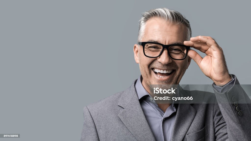 Smart businessman with glasses posing Smart mature businessman with glasses posing on gray background, he is smiling at camera Portrait Stock Photo