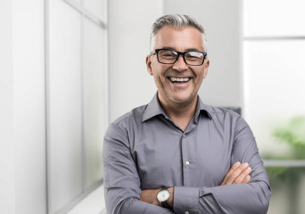 Confident businessman posing in the office Confident businessman posing in the office with arms crossed, he is smiling at camera ceo photos stock pictures, royalty-free photos & images