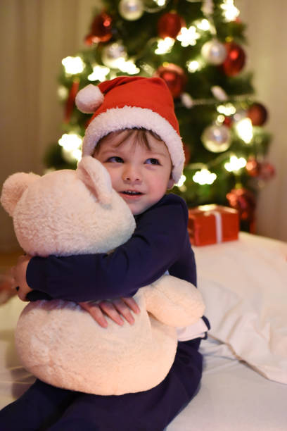 istock Little boy hugging  teddy bear in front of Christmas tree 891422800
