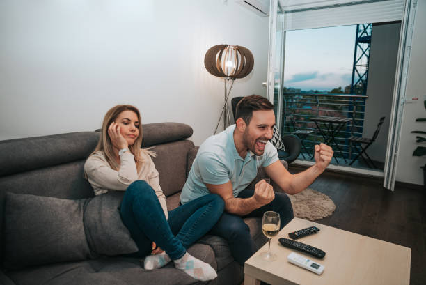 istock Man watching football, while his girlfriend is sitting besides him bored. 891422890