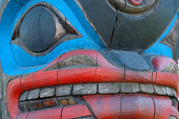 Close-up of a red, black and blue colored wooden totem Close-up and part of a totem pole with blue eye and teeth sticking out. The totem pole is one of several totem-poles standing on and around the marketplace in the city center of Duncan, Vancouver island, Canada duncan british columbia stock pictures, royalty-free photos & images