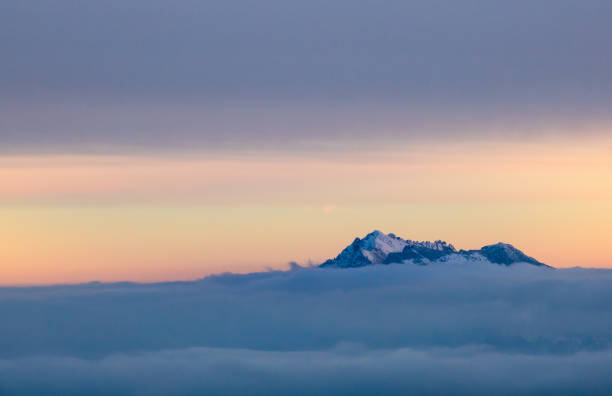 single mountain peak above the clouds in a sunrise sky in early morning in the Swiss Alps