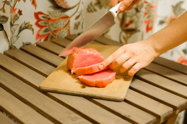 Woman cutting fresh salmon fillet on wooden board