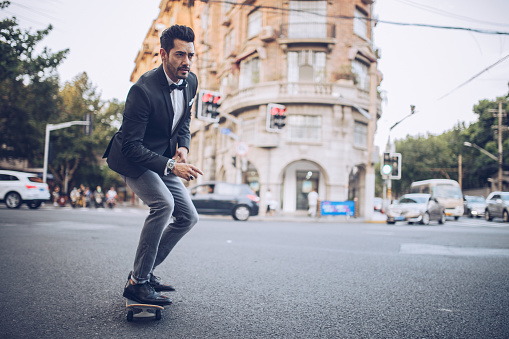 Handsome modern man standing on the street in big city, riding skateboard.