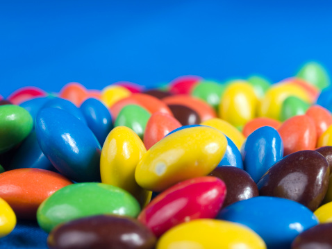 Top view of an assortment of multicolored candies, lollipops and jelly beans background. All the candies are at the center of the image making a horizontal stripe shape and leaving a useful copy space at the top and at the lower side of the image on a withe background.  Studio shot taken with Canon EOS 6D Mark II and Canon EF 24-105 mm f/4L