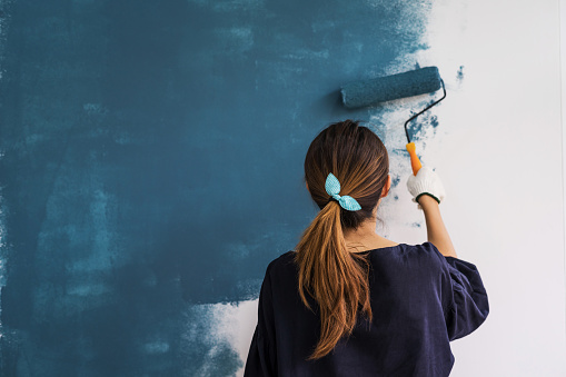 Young asian happy woman painting interior wal