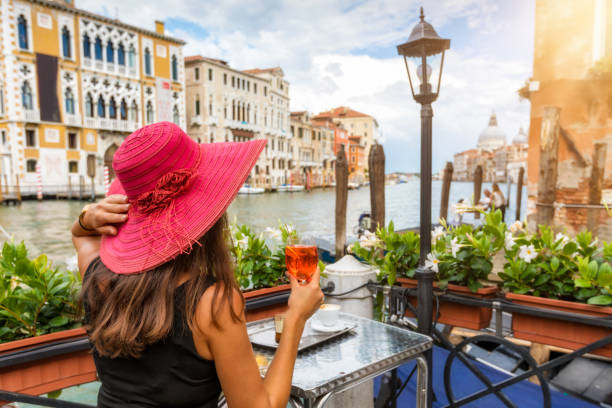 Elegant woman enjoys an aperitif sitting next to the Canale Grande Elegant woman with a red hat enjoys an aperitif sitting next to the Canale Grande in Venice, Italy gondola traditional boat photos stock pictures, royalty-free photos & images