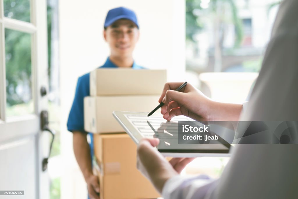 Delivery, mail, people and shipping concept. delivery, mail, people and shipping concept.Young woman sign in digital mobile phone after receiving parcel from courier at home. Delivering Stock Photo