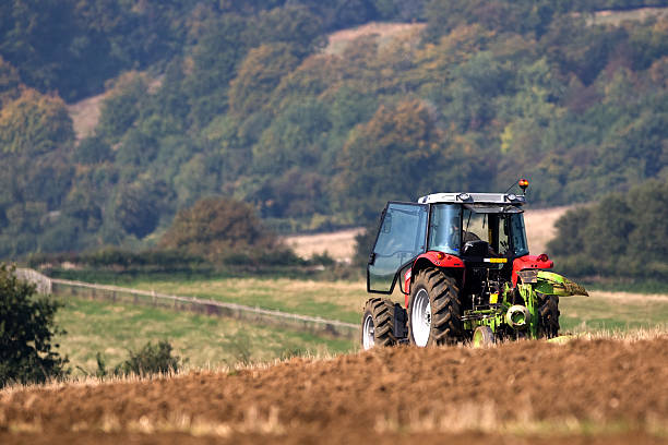 Tractor ploughing a field with a forest in the distance stock photo