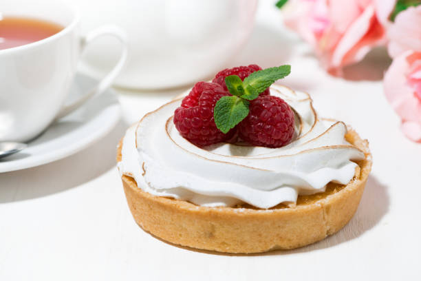 sweet dessert tartlet with meringue and fresh raspberry on white table, closeup